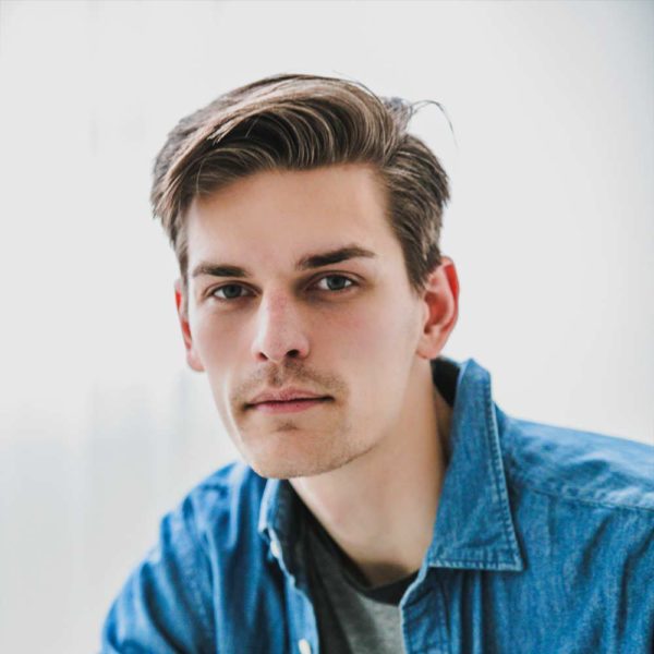 t007 A close up photo of a person looking at the camera, wearing a blue jacket, against a white background.