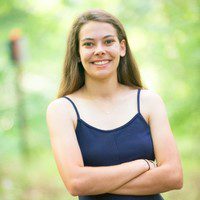 A photo of someone in a blue shirt with their arms crossed, looking at the camera.