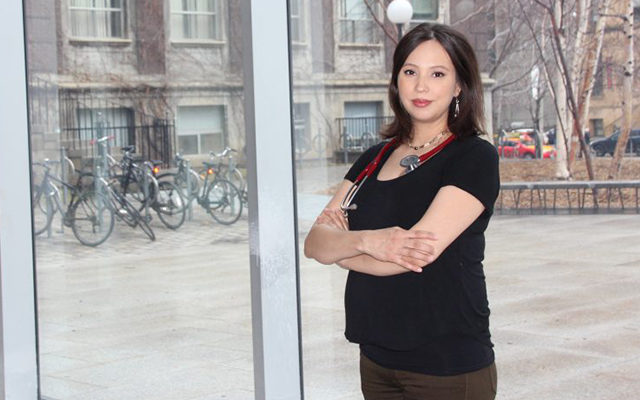 A person with a stethoscope and their arms crossed, with a window behind them.