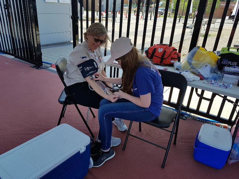 Someone in a blue shirt is seen taking the blood pressure of another person. Both people are seated.