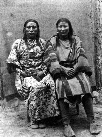 A black and white photo of two people seated beside one another, looking at the camera.