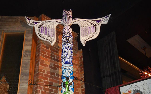 A tall, multicoloured Totem pole, with a brick wall in the background.