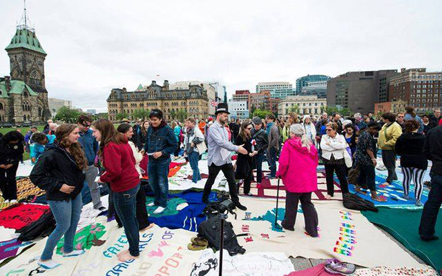 Many people gathered on Parliament Hill, standing on top of blankets on the ground, which have been designed.