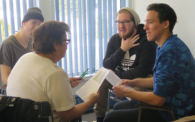 Four people are seated, holding papers, having a discussion.
