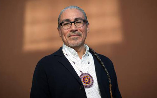 A photo of Harlan Pruden, in front of an orange background.